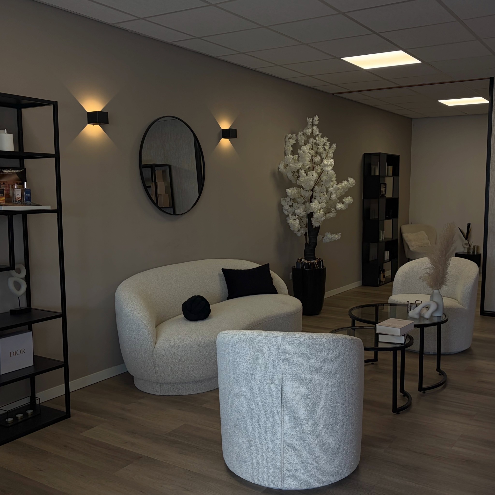 De lounge van Fully Fabulous: greige muren, witte bouclé fauteuils, een ronde spiegel en een bloesemboom